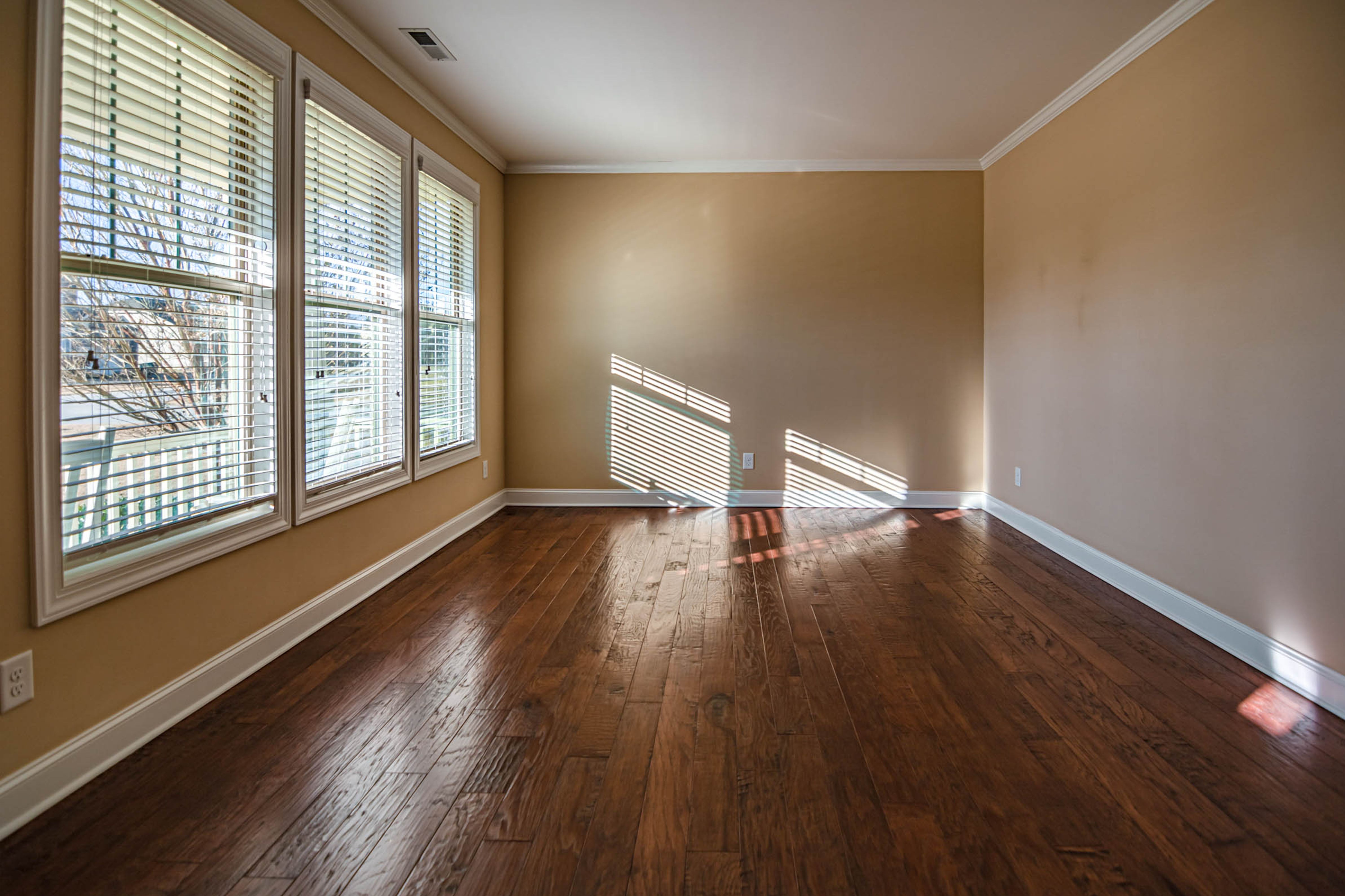 Sunlit empty rental room with hardwood floors and large windows